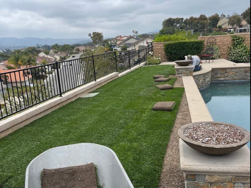 Rolls of sod in a wheelbarrow beside a hillside pool yard